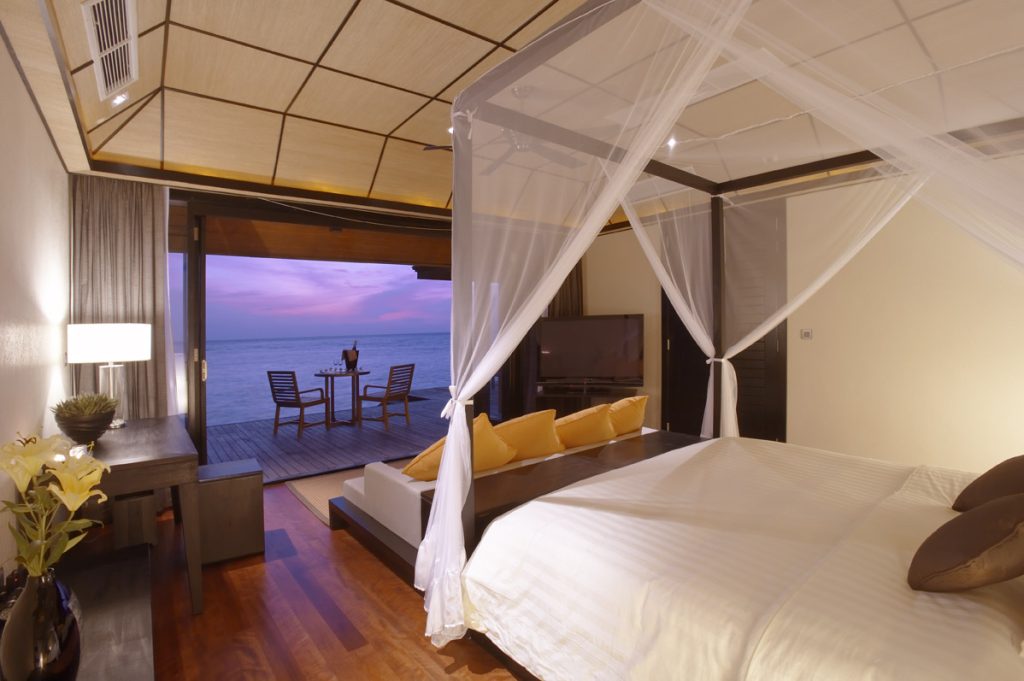 Zimmer der Sunset Water Suite mit Himmelbett, Holzboden, Terrasse und Ozeanblick bei Sonnenuntergang auf den
