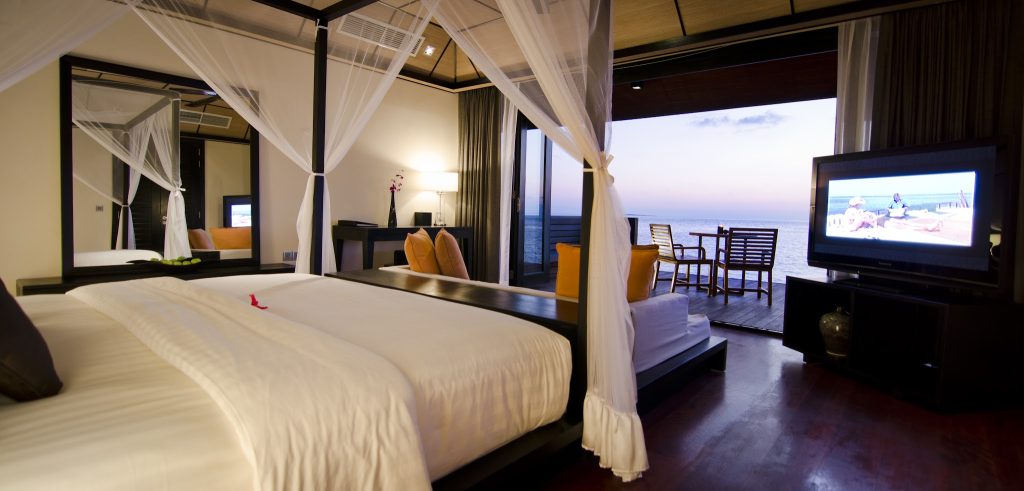Zimmer der Sunset Water Suite mit Himmelbett, dunklen Holzmöbeln und Meerblick auf den