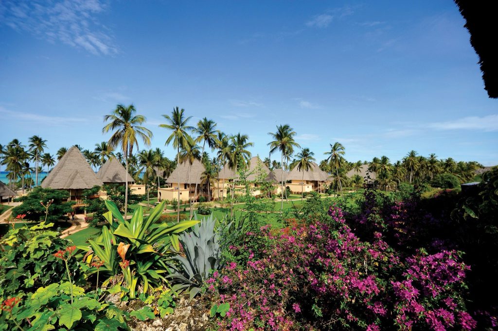 Tropische Resort mit strohgedeckten Bungalows und hohen Palmen vor blauem Himmel in Sansibar