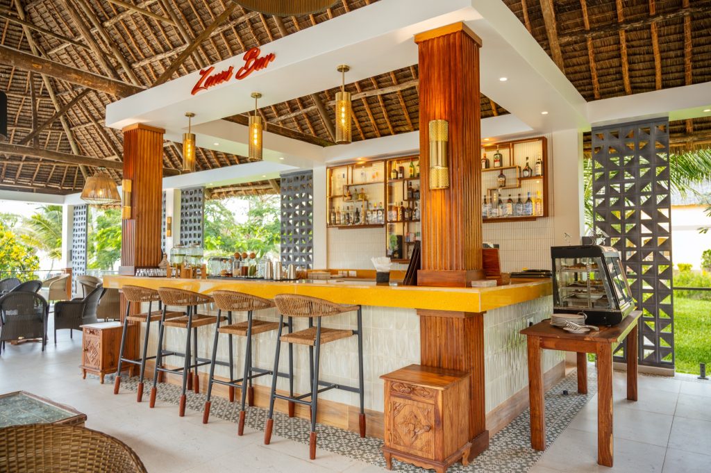 Offene Bar mit gelber Arbeitsplatte, Holzsäulen und geflochtenen Hockern im Neptune Pwani Beach Resort & Spa