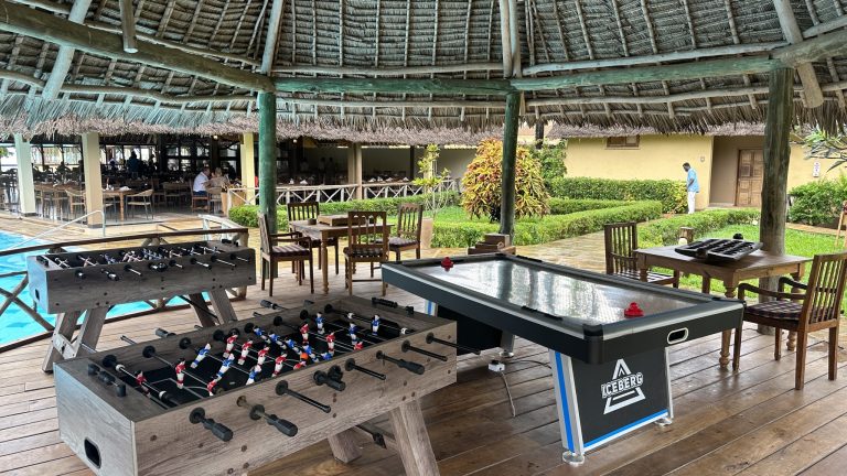 Überdachter Außenbereich mit Holzspieltischen und Holzmöbeln auf Terrasse des Neptune Pwani Beach Resort & Spa