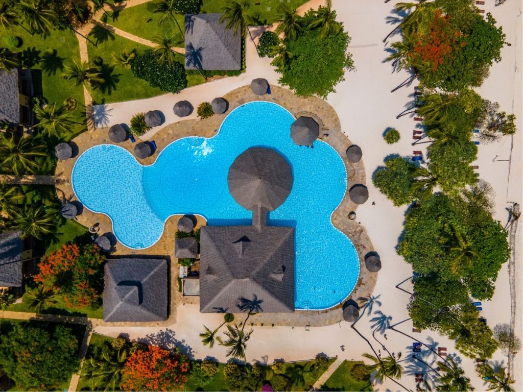 Vogelperspektive auf Neptune Pwani Beach Resort & Spa mit organisch geformtem Pool, Strohhütten und grüner Vegetation
