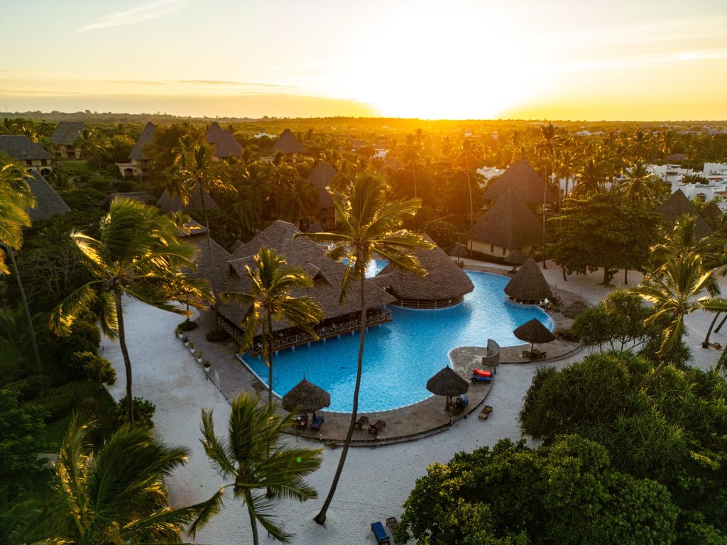 Vogelperspektive auf großen blauen Pool mit Palmen und strohgedeckten Hütten im Neptune Pwani Beach Resort & Spa