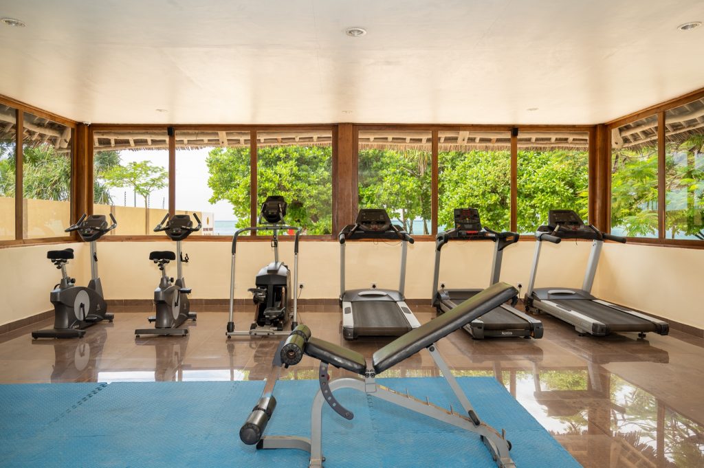 Fitnessraum im Neptune Pwani Beach Resort & Spa mit Fahrradergometern, Laufbändern und großen Fenstern zur grünen.