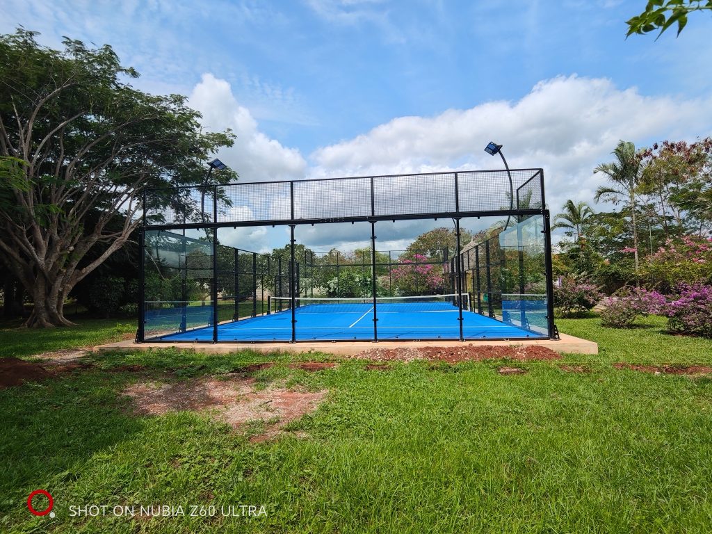 Hellblauer Padelplatz im Neptune Pwani Beach Resort & Spa mit Metall- und Glaszaun und grüner Umgebung in Sansibar
