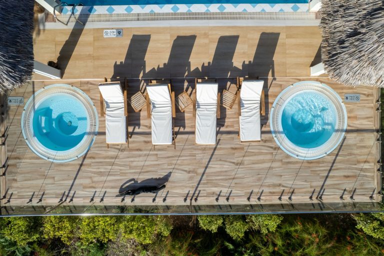 Vogelperspektive auf Terrasse mit zwei runden blauen Whirlpools, Liegestühlen und Holzplanken im Neptune Pwani Beach Resort.