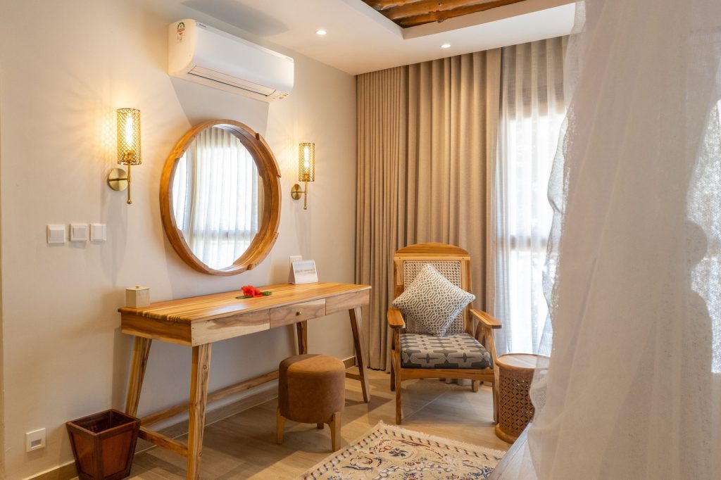 Hotelzimmer Deluxe Room mit hölzernem Schreibtisch, rundem Spiegel und warmen Erdtönen im Neptune Pwani Beach Resort & Spa