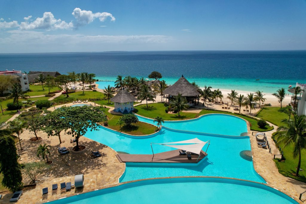 Blick auf Royal Zanzibar Beach Resort mit mehreren blauen Pools, Steinwegen, Palmen und türkisfarbenem Meer im Hintergrund