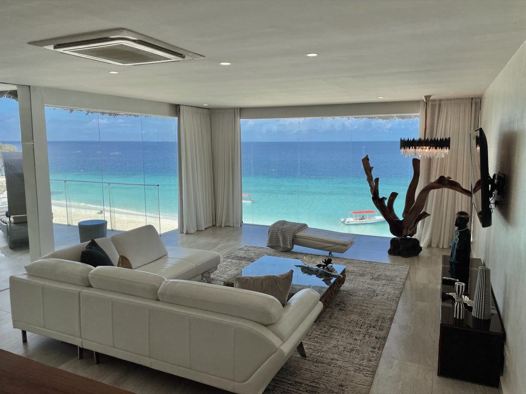 Weißes Ledersofa und Glastisch in Royal Suite Wohnzimmer mit großem Fenster und Blick auf den Ozean und ein Boot