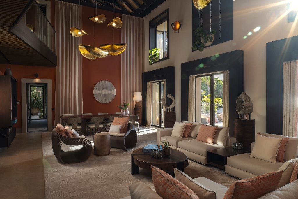 Hotelzimmer mit hohen Decken, großen Fenstern, modernen Sesseln und Sofas mit roten Kissen auf den