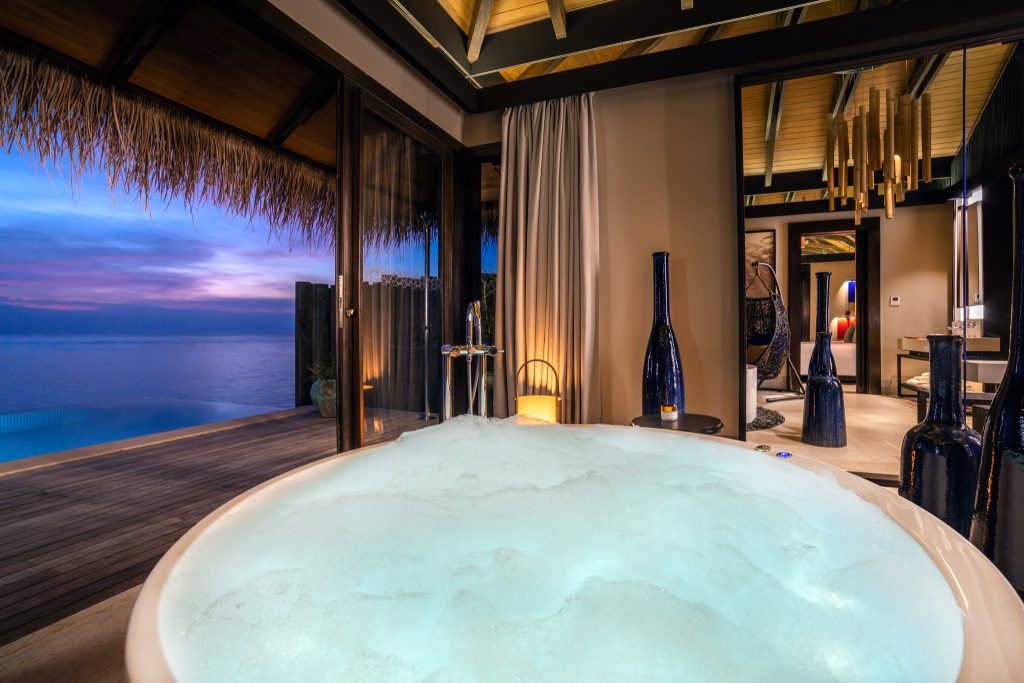 Zimmer der Deluxe Water Pool Villa mit Whirlpool, Terrasse, Infinity-Pool und Meerblick bei Dämmerung auf den