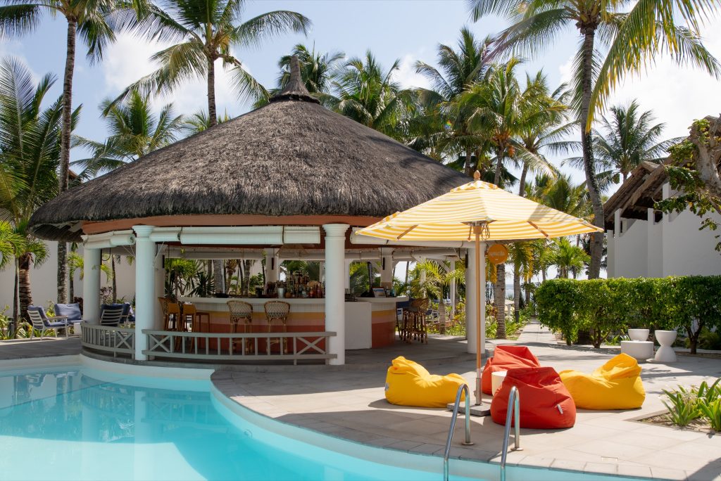 Außenansicht der Veranda Palmar Beach Hotel Bar mit rundem Strohdach, bunten Sitzsäcken und Sonnenschirm am Pool