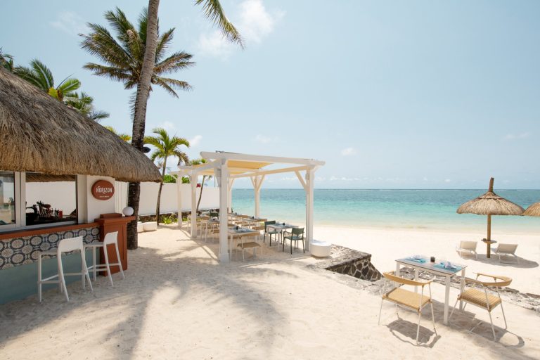 Offener Pavillon aus weißem Holz mit Tischen und Stühlen aus Metall und Rattan, Bar Horizon mit Strohdach am Strand