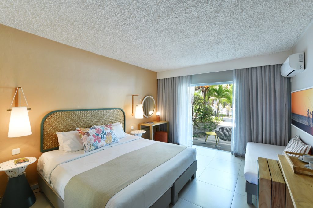 Helles Comfort Garden Zimmer im Veranda Palmar Beach Hotel mit Doppelbett, geflochtenem Kopfteil und Glas-Schiebetür.
