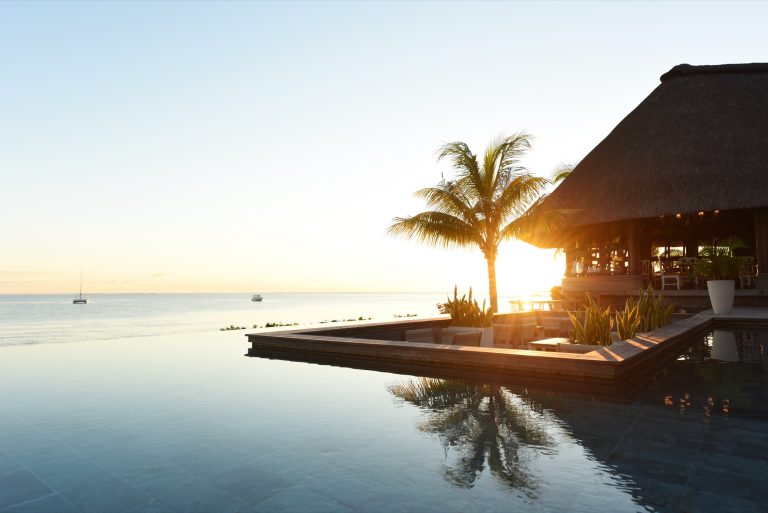 Infinity-Pool vor Strohdach-Gebäude mit Palmen und Holzdeck im Restaurant Ile de France, Mauritius