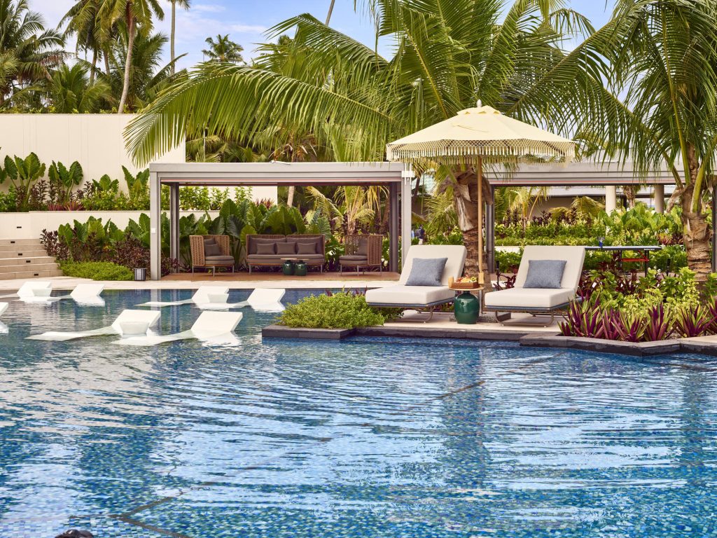 Poolbereich mit weißen Sonnenliegen, Holzmöbeln und Palmen im Waldorf Astoria Seychelles Platte Island
