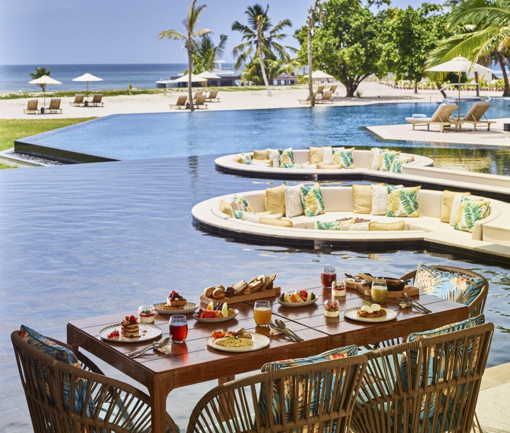 Außenterrasse Restaurant La Perle mit Holztisch, geflochtenen Stühlen, Infinity-Pool und Meerblick auf den