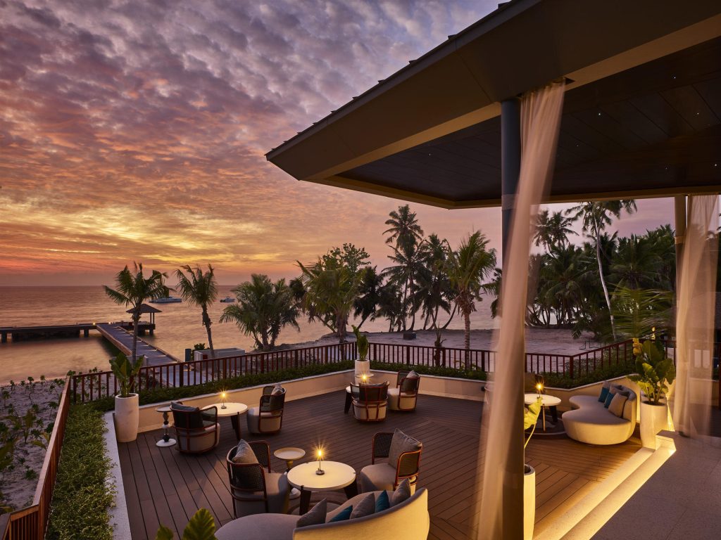 Terrasse des Restaurants Lalin mit Holz- und Stoffmöbeln, Stoffvorhängen und Meerblick bei Sonnenuntergang