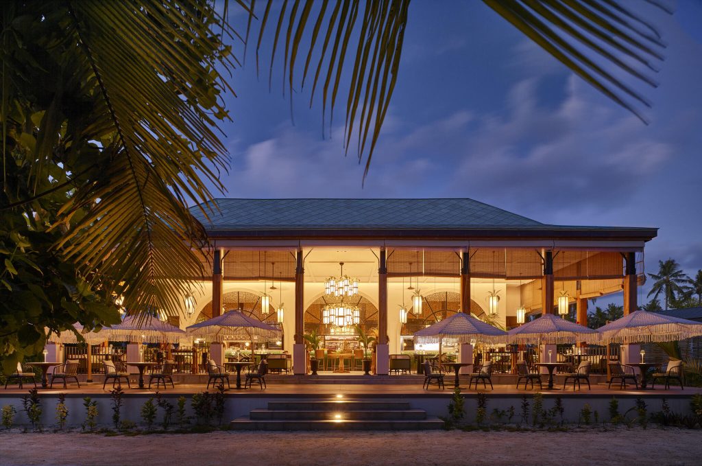 Außenansicht des Restaurants Maison des Epices bei Dämmerung mit Palmen, Holzterrasse