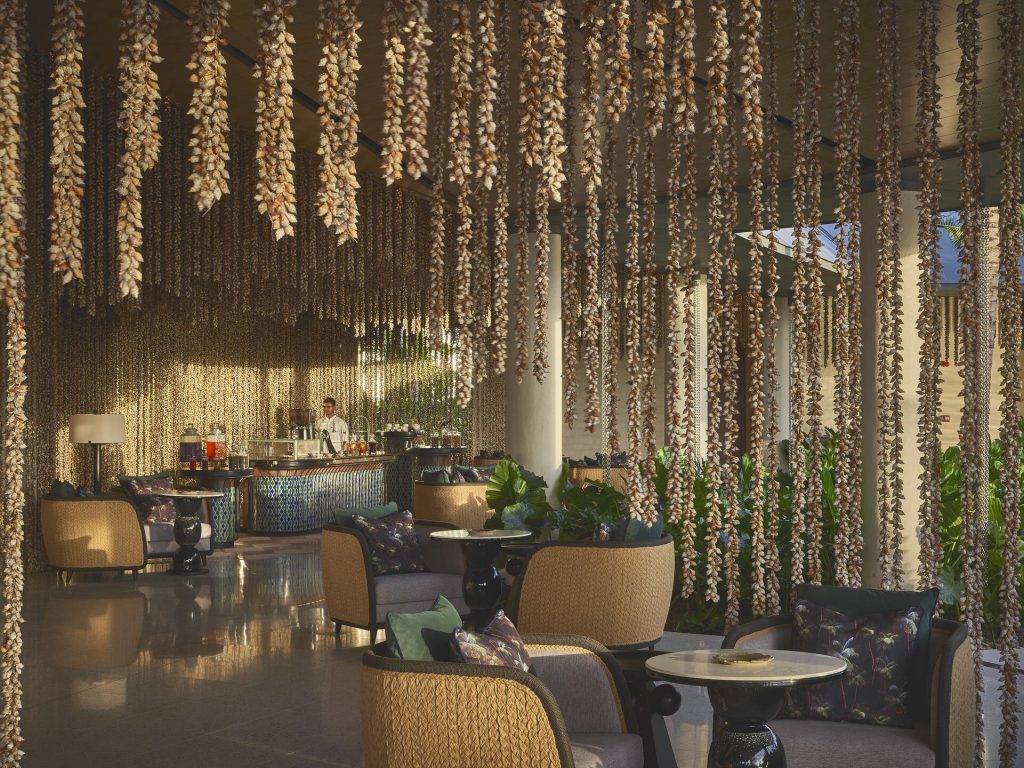 Hotel-Lounge mit hängender Dekoration, Holzsesseln und Bar im Hintergrund im Waldorf Astoria Seychelles