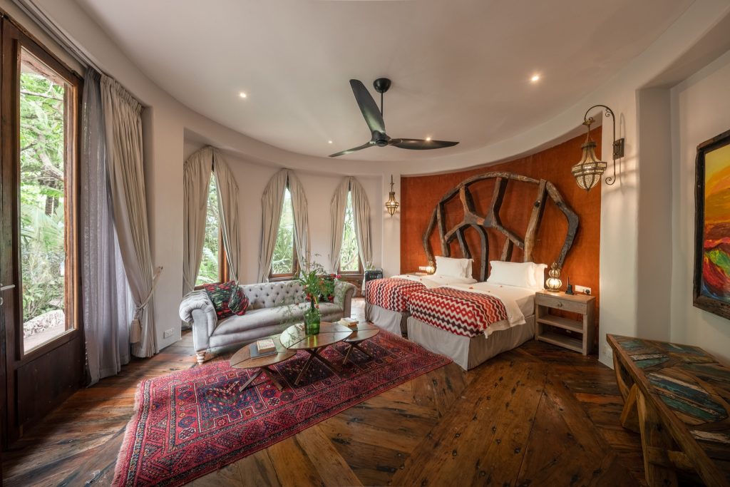 Hotelzimmer in Xanadu Villas mit rotem Wandakzent, grauem Sofa, Holzboden und großen Fenstern in Sansibar
