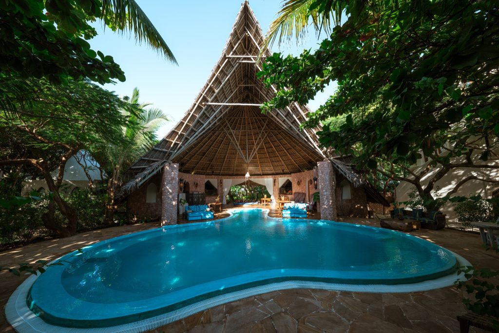Poolbereich der Xanadu Villas mit hellblauem Wasser und Dach aus Holz und Stroh, umgeben von grüner Vegetation