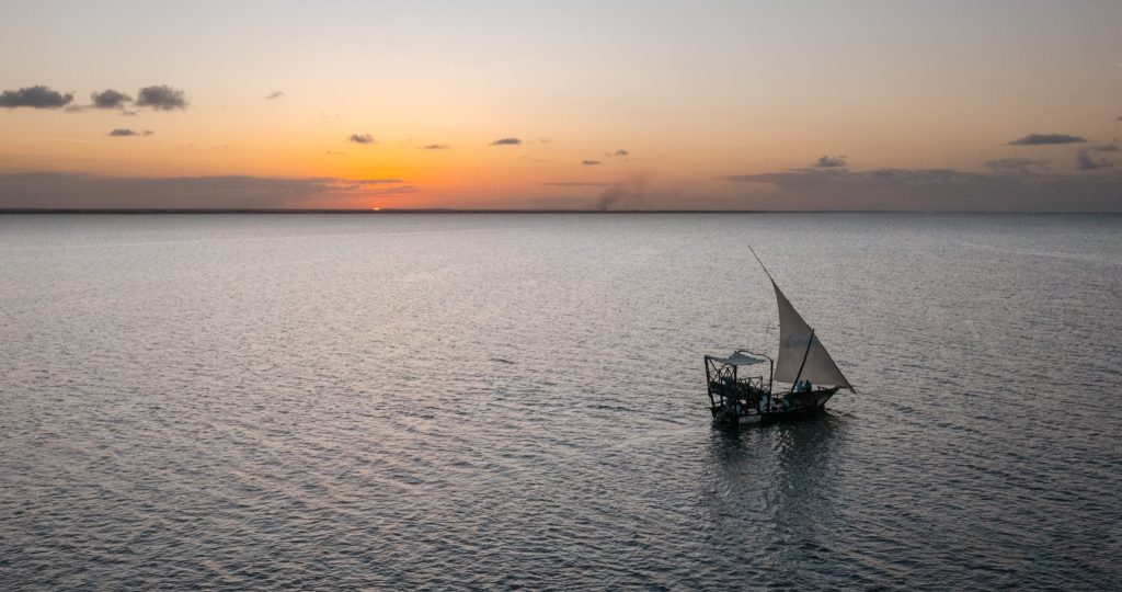 Kleines hölzernes Segelboot mit weißem Segel treibt auf ruhiger Wasseroberfläche bei Sonnenuntergang