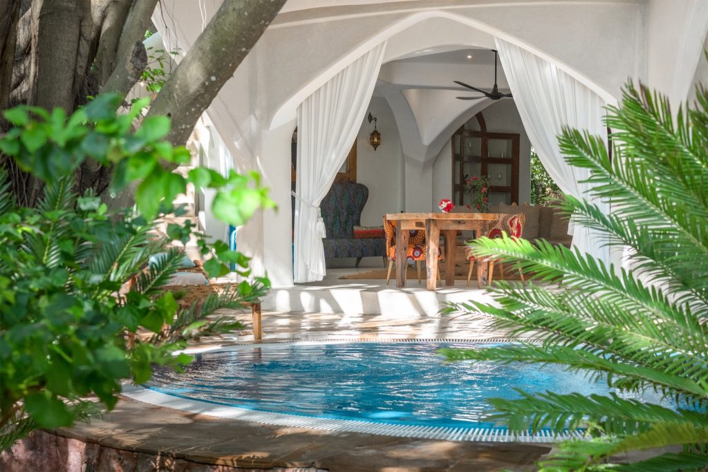 Offener Bereich der Villa Alfajiri mit kleinem Pool, weißem Vorhang und Holztisch mit bunten Stühlen