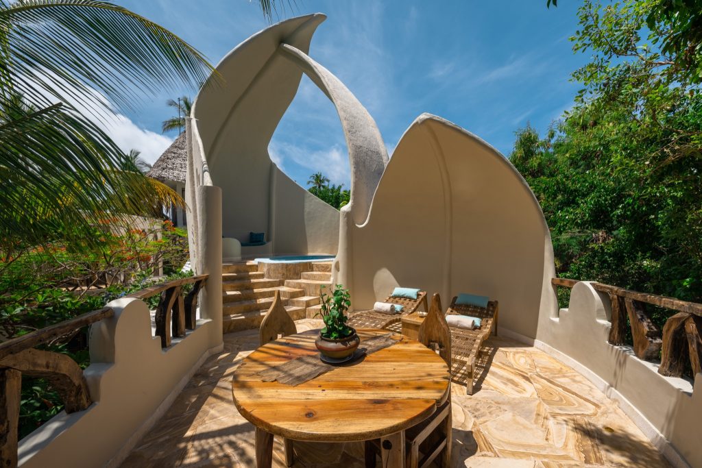 Terrasse der Villa Kimwondo in den Xanadu Villas mit Holztisch, zwei Holzliegen, Betonstruktur und kleinem Pool