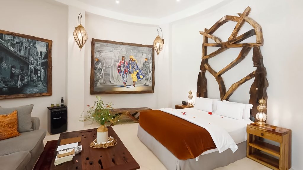 Hotelzimmer Villa Kimwondo mit großem Bett, verwobenem Holz-Kopfteil, Sofas, Tisch und warmen Erdtönen