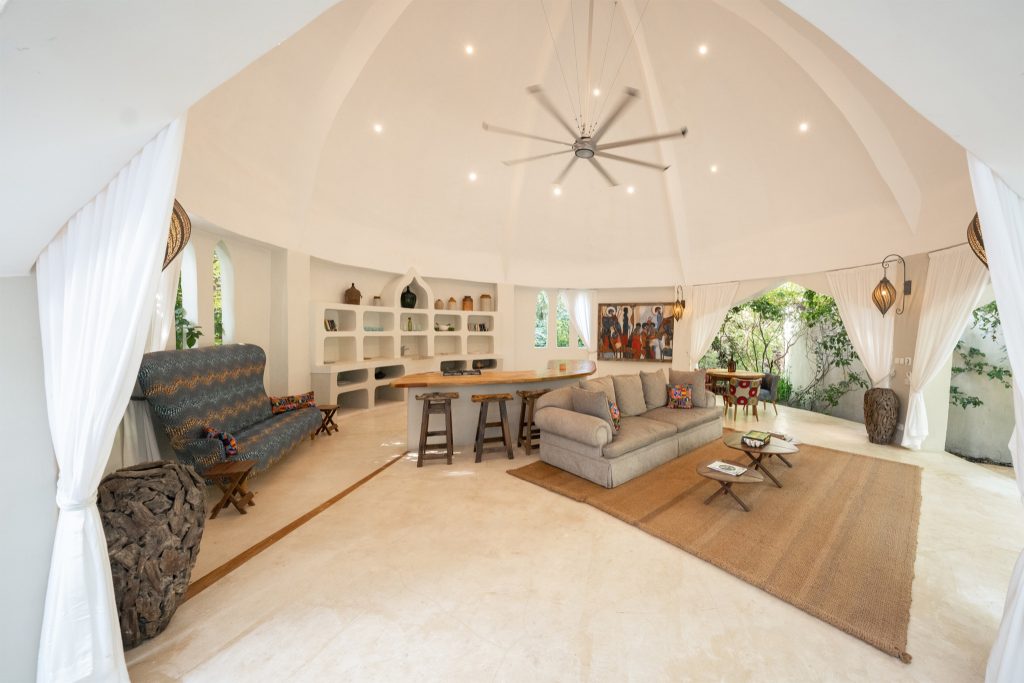 Heller, geräumiger Raum in der Villa Korongo mit Sofa, Holzhockern, hellem Teppich und Tageslicht