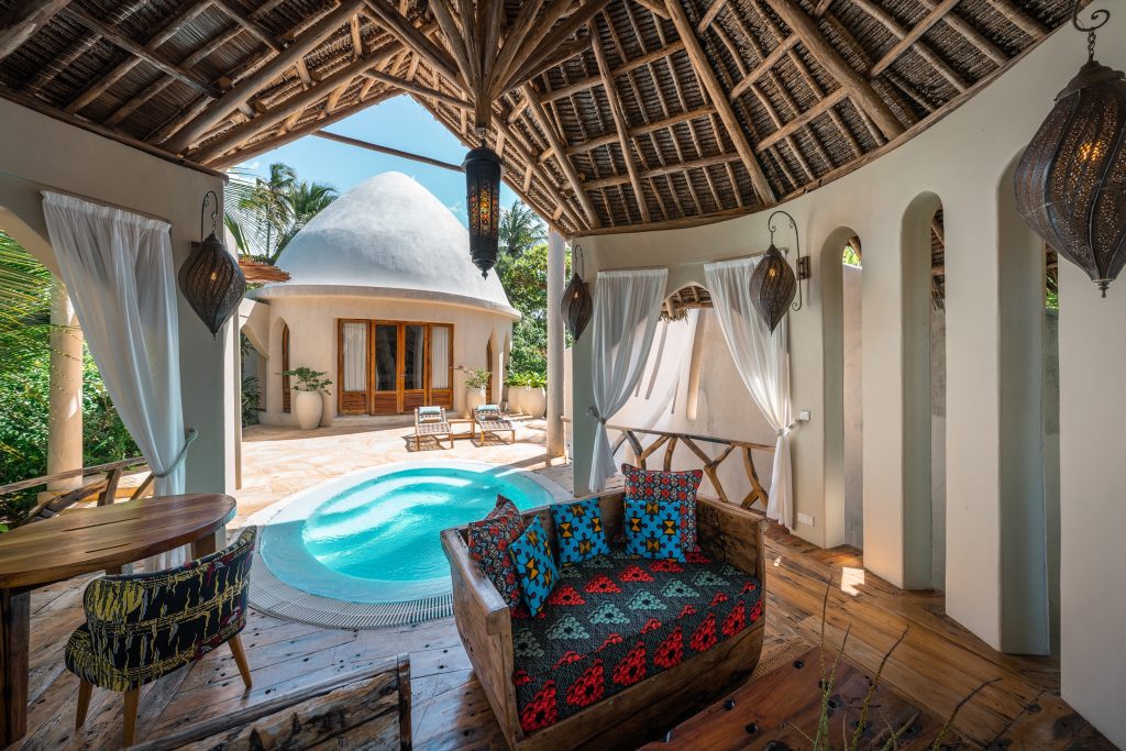Outdoor-Lounge der Villa Mawimbi mit rundem Pool, Holzmöbeln und geflochtenem Dach bei Tageslicht