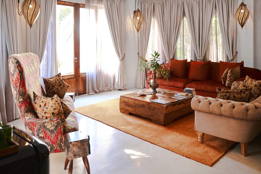 Wohnzimmer der Villa Mawingu in Xanadu Villas mit rotem Sofa, Holztisch, orangefarbenem Teppich und gemusterten Kissen