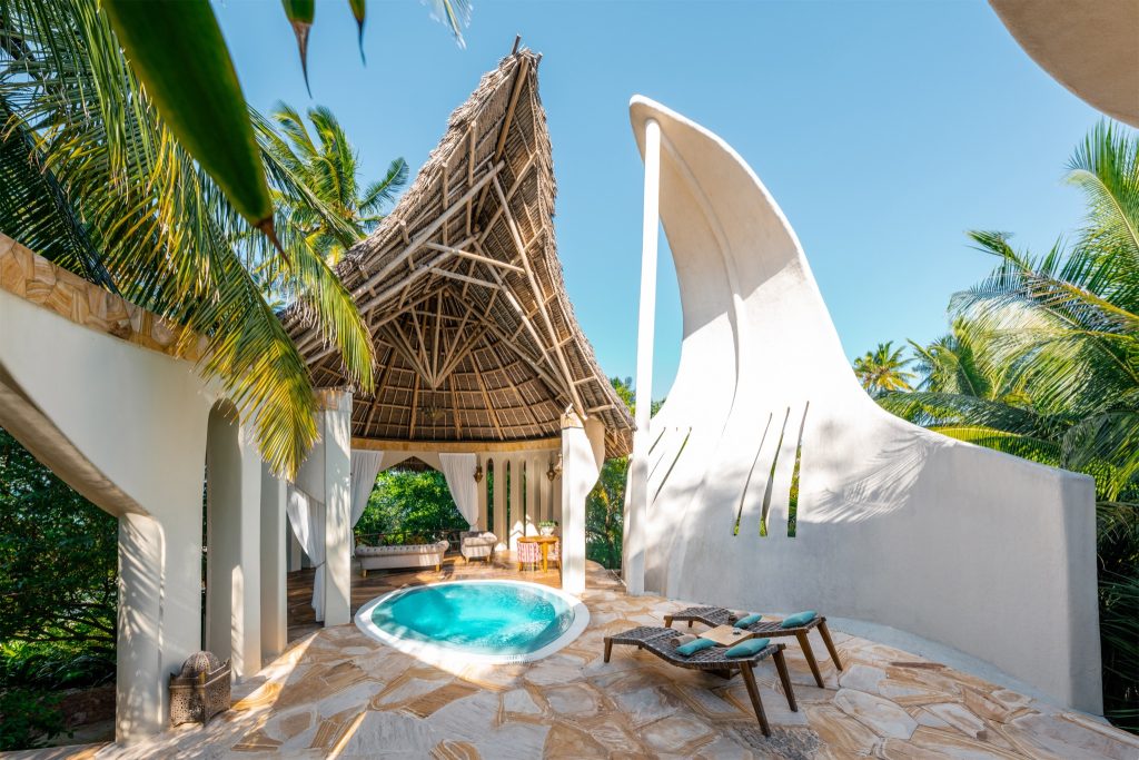 Exotischer Außenbereich mit rundem Pool, helle Steinfliesen, Holzmöbel und strohgedecktem Pavillon bei Tageslicht