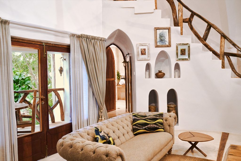Wohnlicher Hotelraum Villa Mbingu mit großen Fenstern, Holzelementen und beigefarbenem Sofa in Xanadu Villas Sansibar