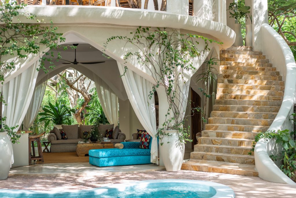 Lounge-Bereich der Villa Mbingu in Xanadu Villas mit Sofas, farbigen Kissen, Steintreppe und Pool in Sansibar