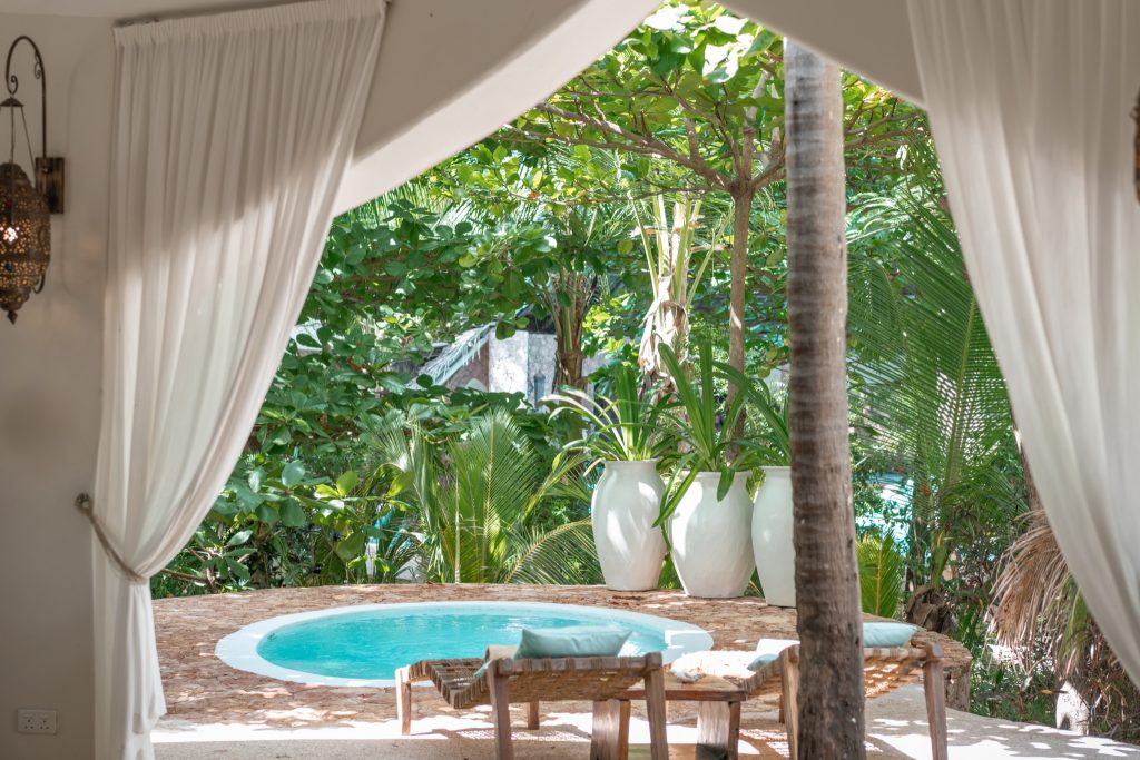 Terrasse der Villa Mlima mit kleinem runden Pool, weißen Vorhängen, Korbstühlen und tropischer Bepflanzung