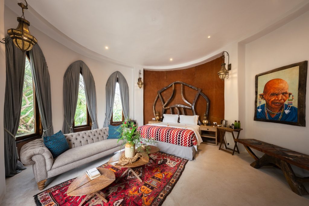 Hotelzimmer Villa Mlima mit großem Bett, dunklem Holz Kopfteil, beigem Sofa und buntem Teppich