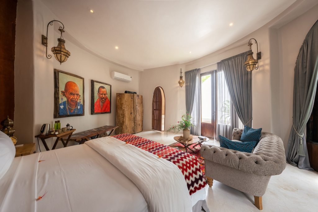 Hotelzimmer Villa Mlima mit massivem Holzschrank, farbenfrohen Porträts, Sofa mit blauen Kissen und Holztisch