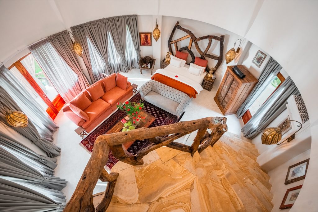 Vogelperspektive auf Villa Nyota Zimmer mit großem Bett, Sitzbank, roter Couch und natürlichen Materialien