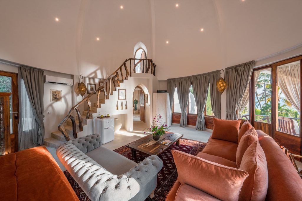 Wohnbereich der Villa Nyota in Xanadu Villas mit orangefarbenen Sofas, grauem Chesterfield-Sofa und handgefertigtem.