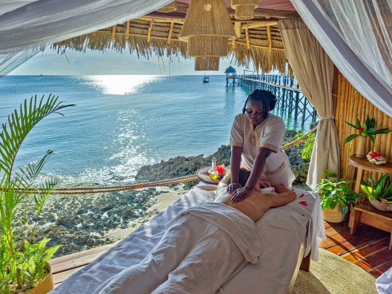 Massage auf weißem Tisch auf Holzplattform im Spa mit Blick auf Meer und Steg in Sansibar