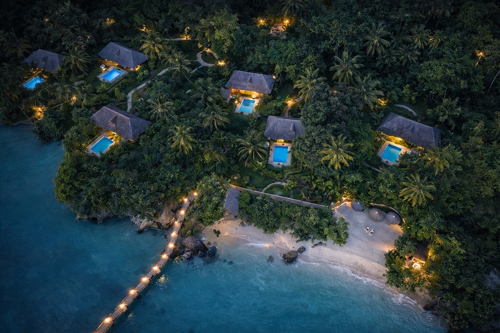 Luftaufnahme von fünf Bungalows mit Strohdächern und privaten beleuchteten Pools im tropischen Wald