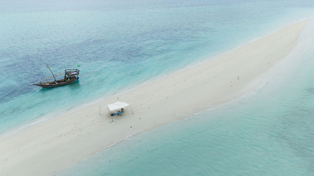 Lange Sandbank mit weißem Pavillon und Liegestühlen neben traditionellem Holzboot im klaren türkisfarbenen Wasser