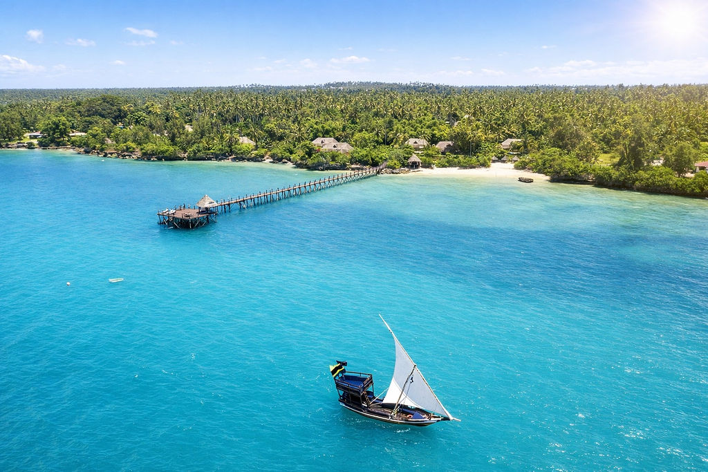 Langer Holzsteg am Strand des Zanzi Resort mit weißem Segelboot und üppigen Palmen in Sansibar