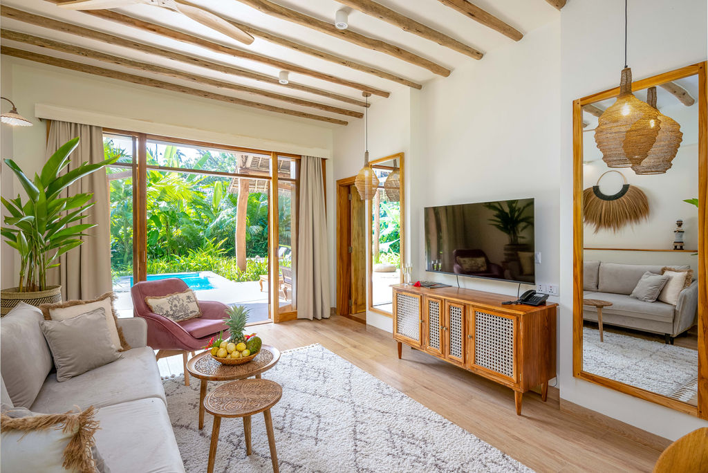 Wohnzimmer der Superior Garden Villa im Zanzi Resort mit Holzmöbeln, großen Glasfenstern und Blick auf Pool und tropischen.