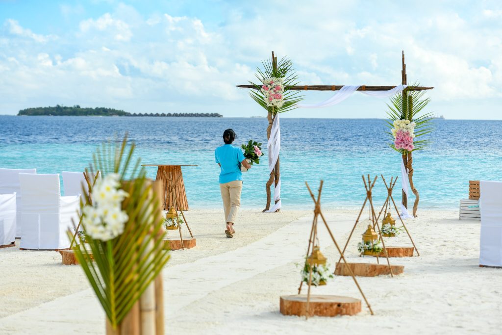 Strandhochzeitszeremonie mit hölzernem Traubogen, weißen Tüchern, pink-weißen Blumen und weißen Stühlen am Banyan Tree.