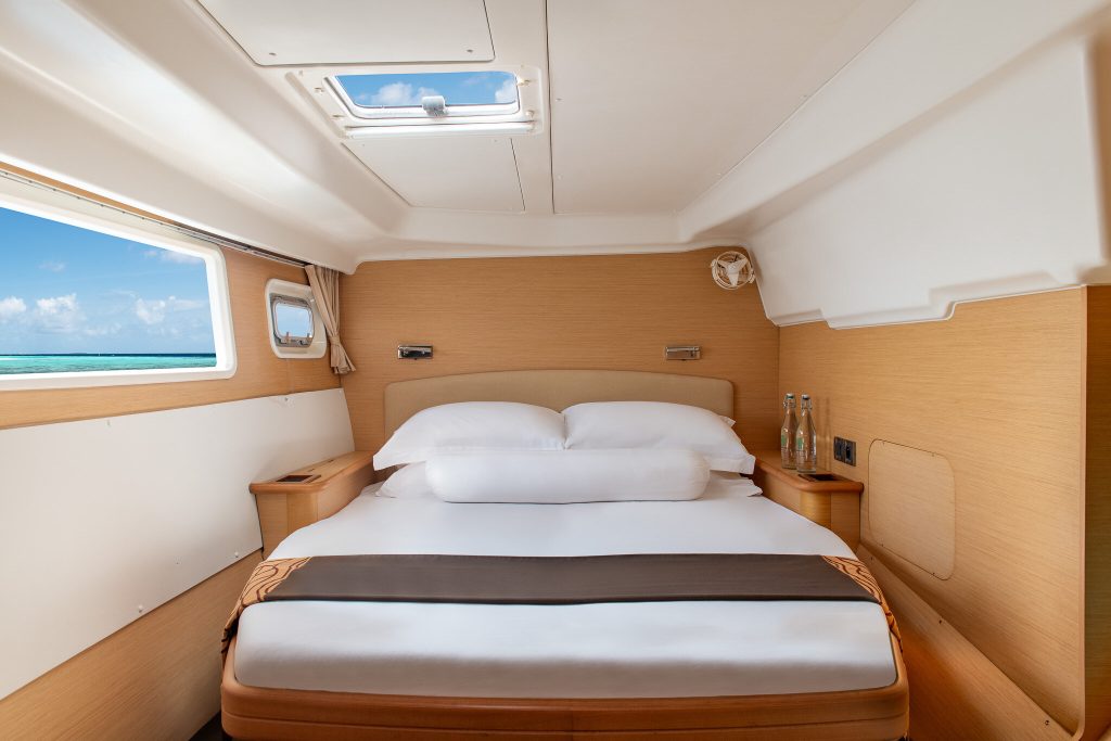 Kleiner Raum mit großem Bett, hellem Holz, zwei Fenstern und Dachfenster mit Blick aufs Meer