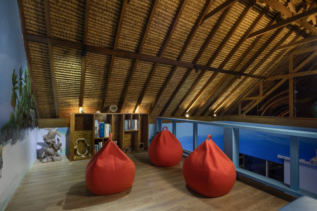 Dachboden-Leseecke im Sport Marine Lab mit roten Sitzsäcken, Holzboden, Holzregal und tropischem Wandgemälde