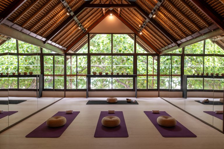 Yoga-Raum im Banyan Tree Vabbinfaru mit lila Yogamatten, geflochtenen Meditationskissen und großen Glasfenstern